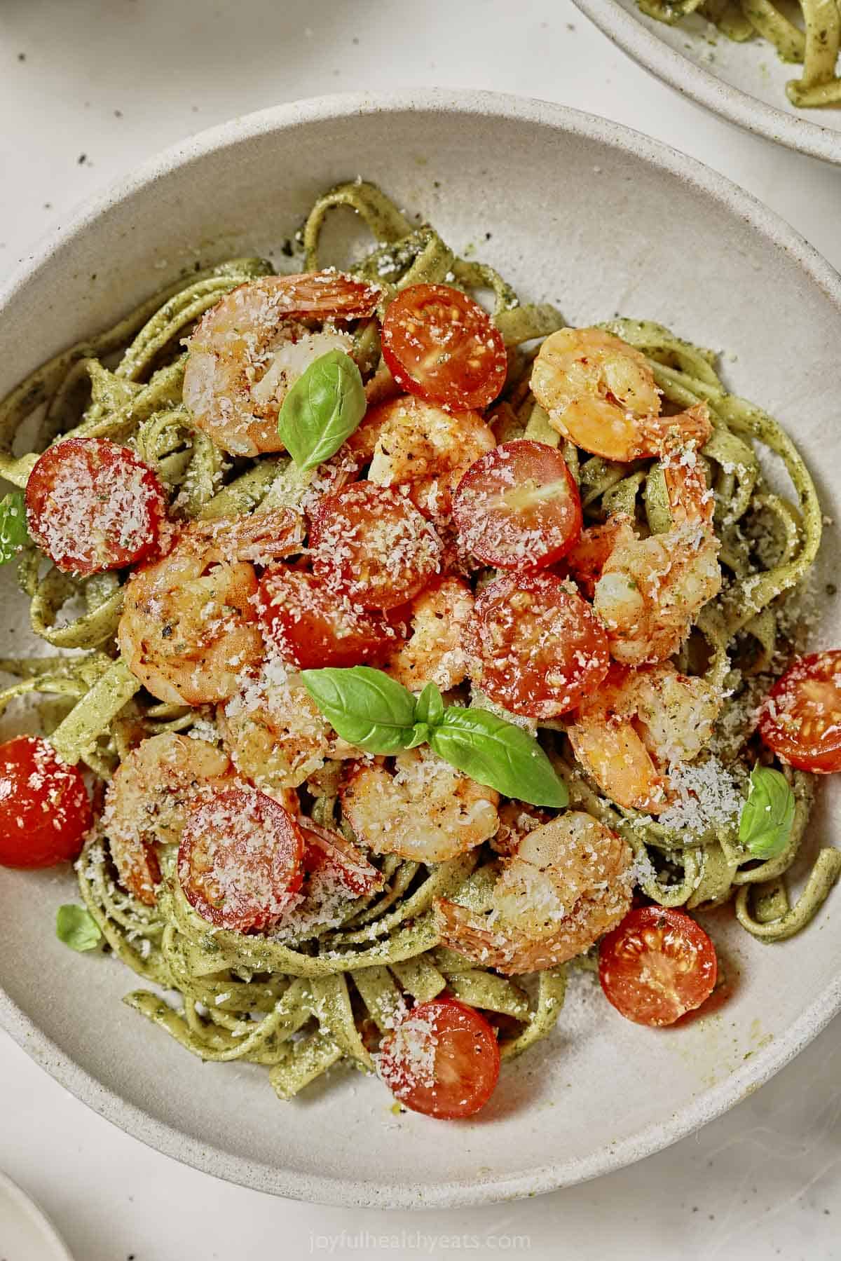 This shrimp and pesto pasta recipe with sweet tomatoes and parmesan cheese is an easy weeknight dinner that can be enjoyed hot or cold. Bowl of shrimp and pesto pasta with juicy tomatoes and parmesan cheese.