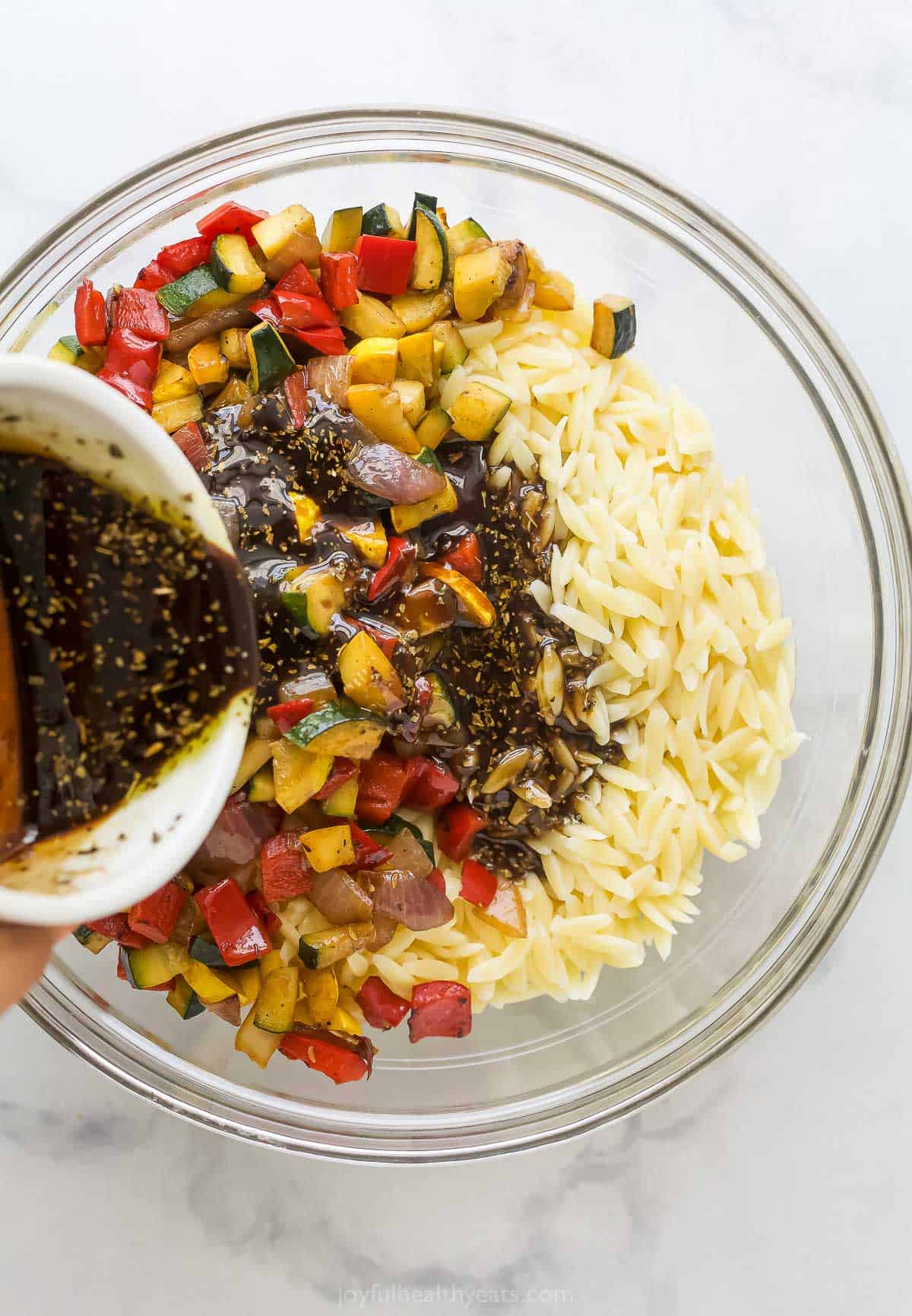 Pouring the dressing into a bowl with orzo and grilled veggies. 