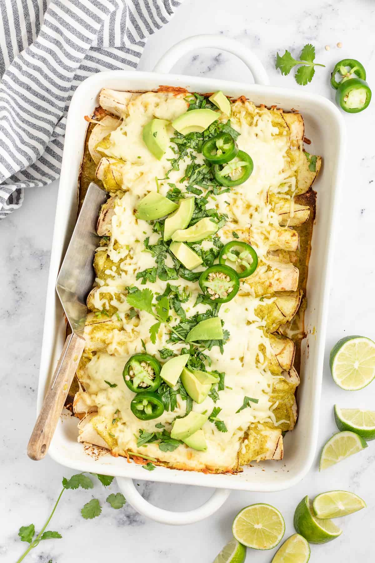 Creamy Chicken Enchiladas Verdes are perfect for big family dinners. They're cheesy and creamy with just the right amount of heat! casserole dish with creamy chicken enchiladas verdes with limes and jalapenos as garnishes