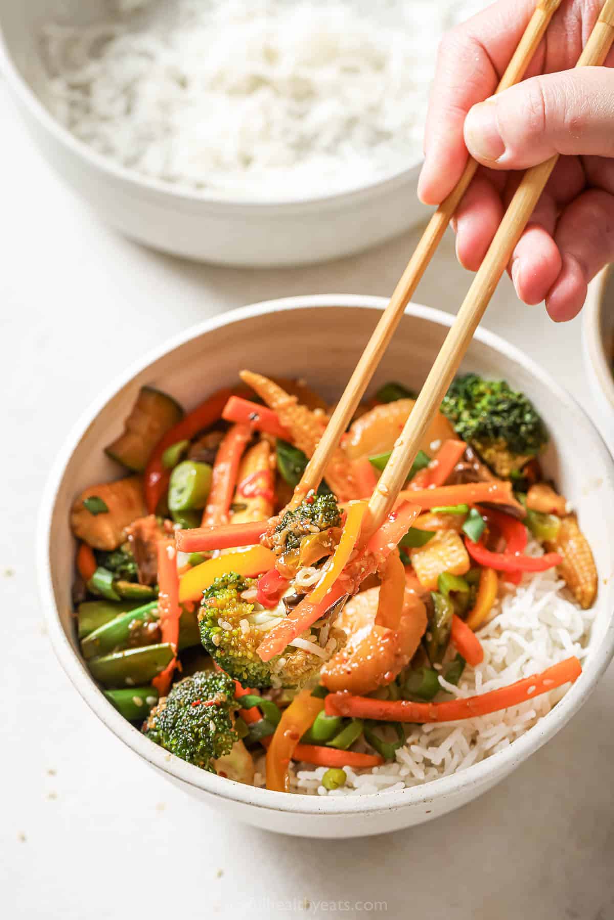 Hand picking up vegetable stir fry from bowl with chopsticks