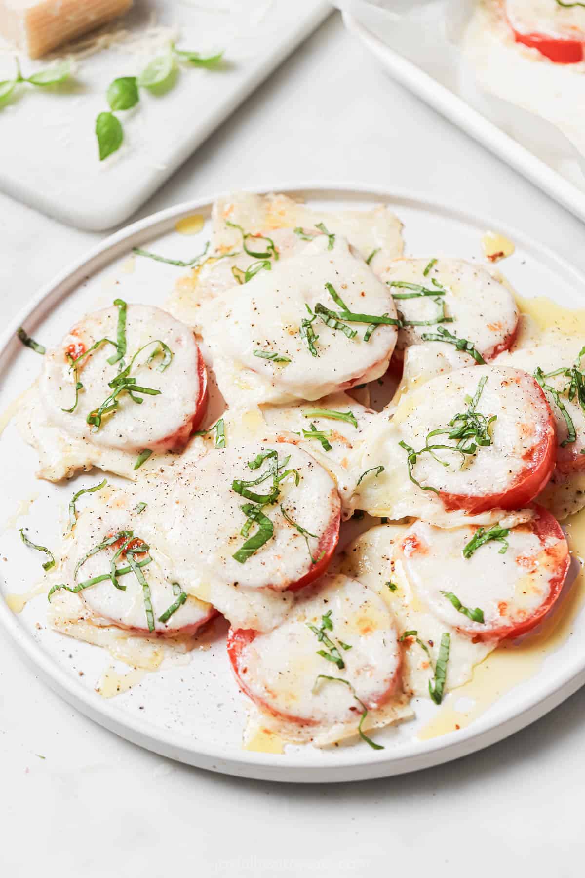 A serving plate of caprese-style tomatoes with fresh basil on top. 