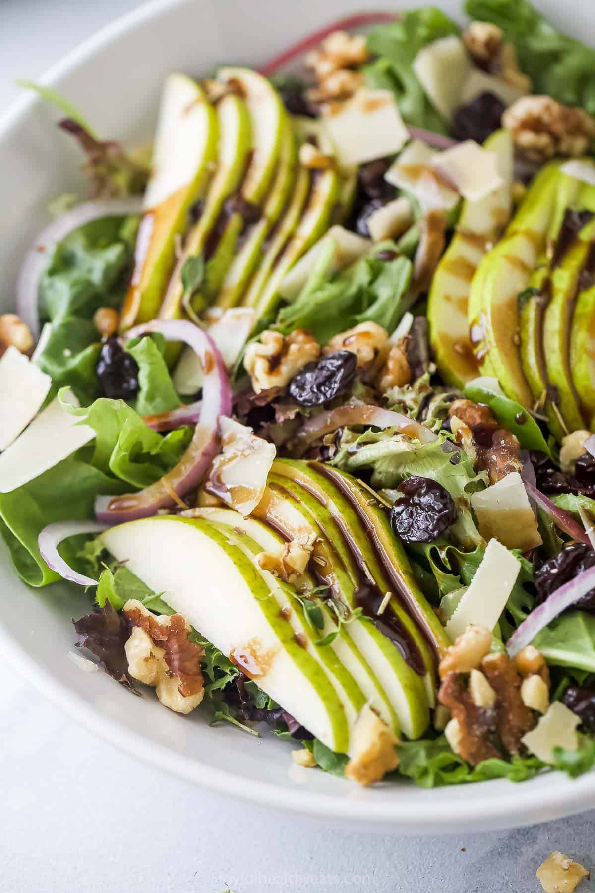 Angled photo of fresh walnut salad with pears, cherries, red onions, and parmesan cheese.