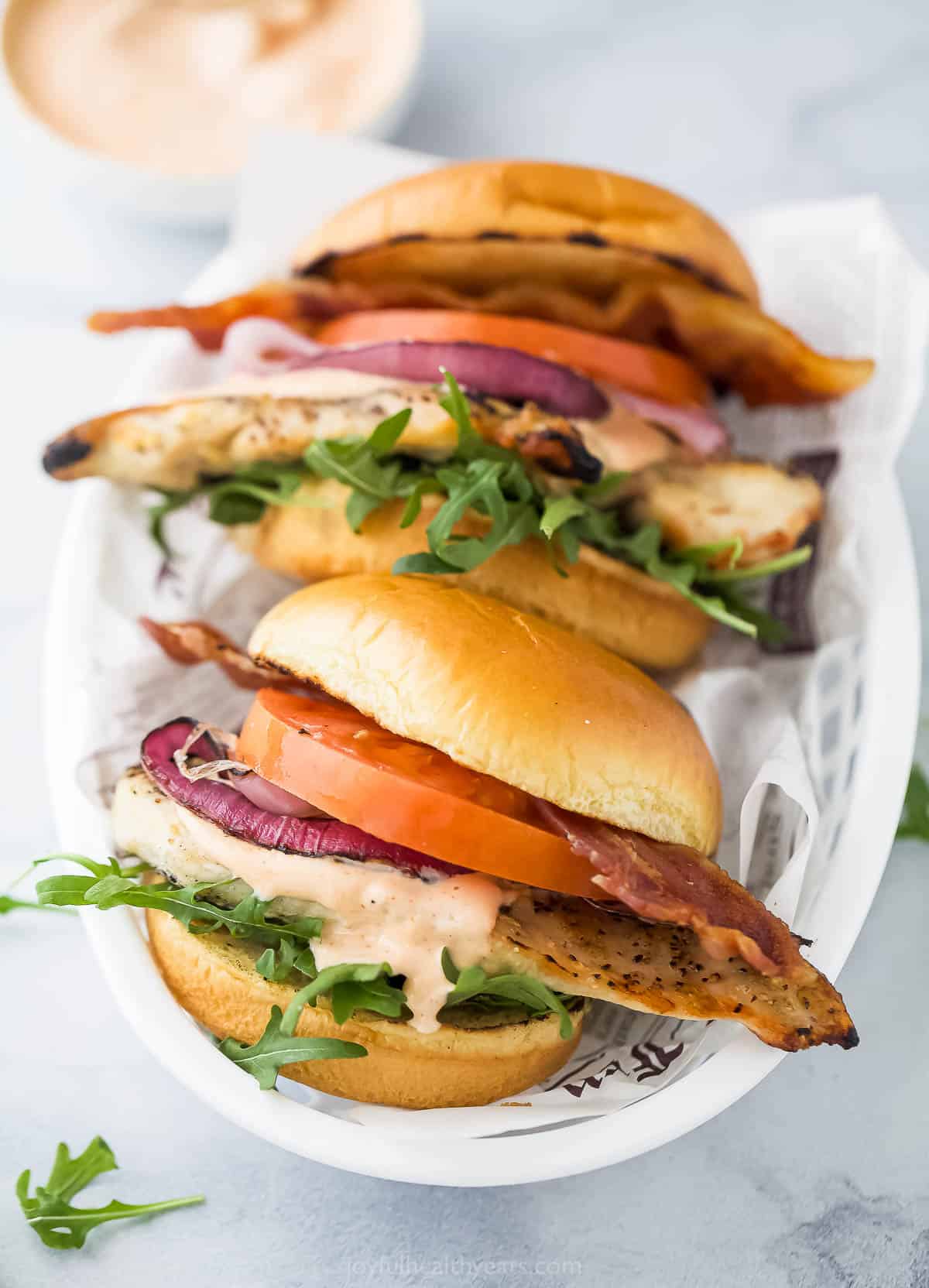 Two grilled chicken sandwiches with a small bowl of chipotle mayo in the background.