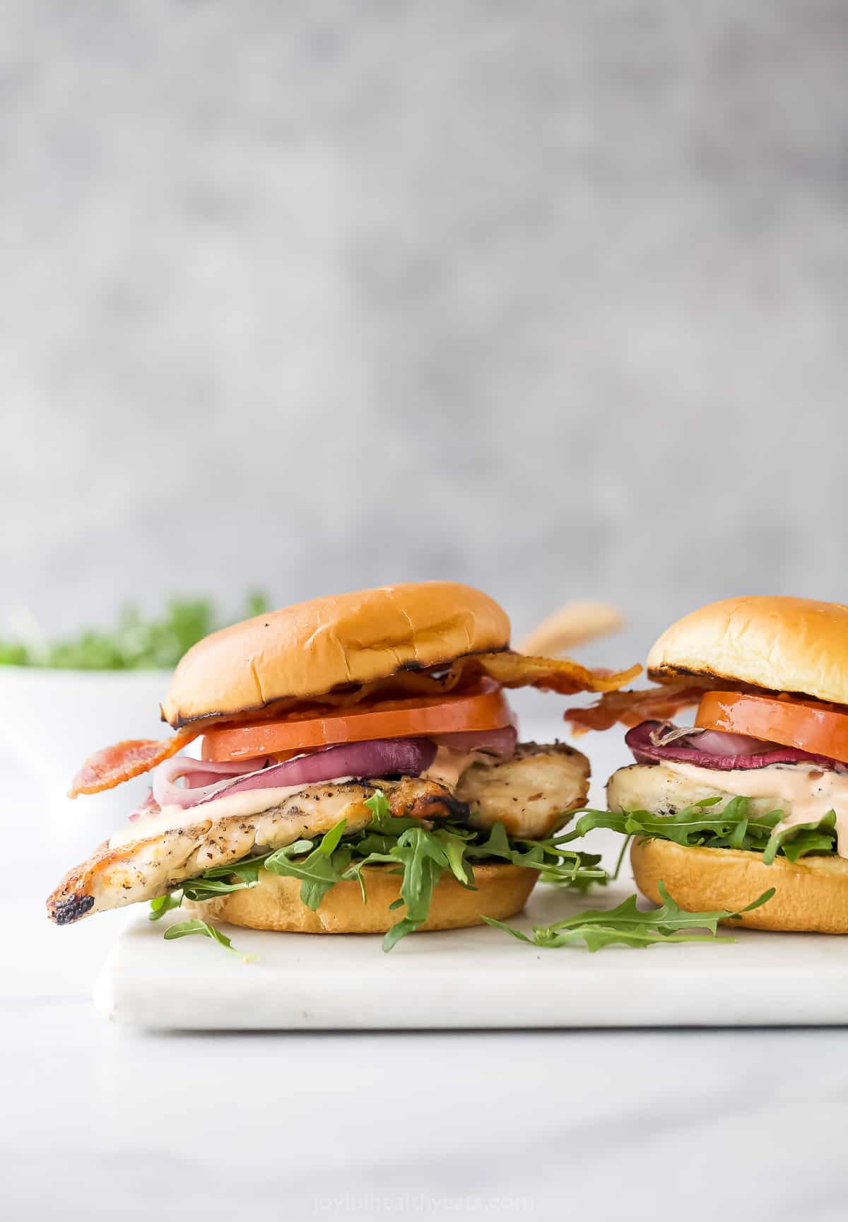 Two sandwiches with chicken, tomatoes, and spring mix salad.