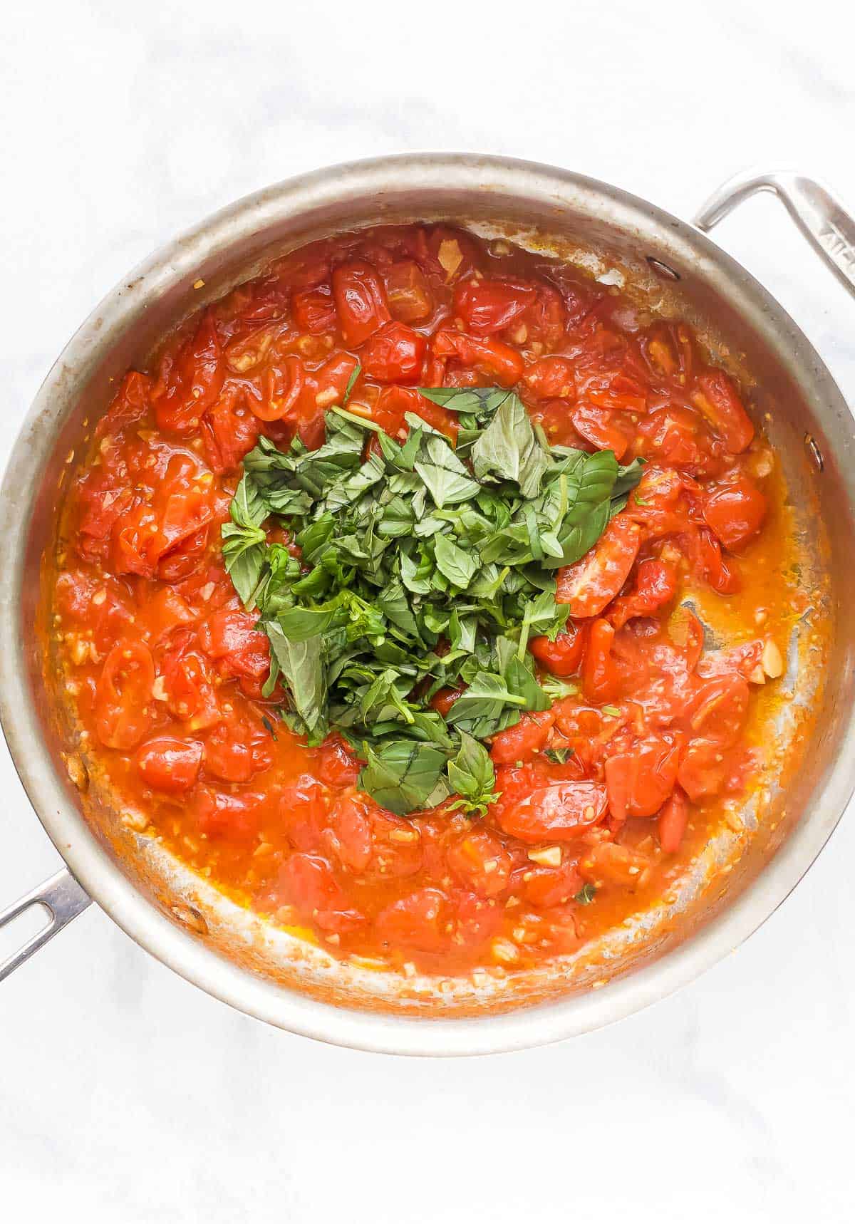 Overhead view of basil leaves added to skillet of pasta sauce