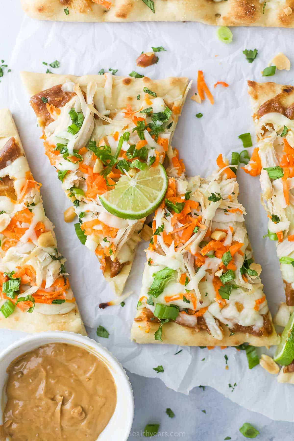This 20-minute Thai chicken pizza recipe with spicy peanut sauce, green onions, carrots, and mozzarella is an easy weeknight dinner. Sliced Thai chicken pizza with fresh cilantro on top.