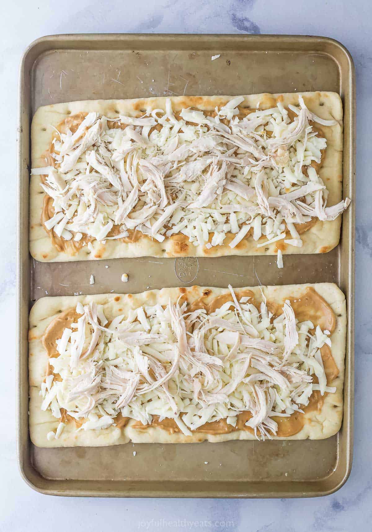 Adding the shredded chicken on top of the cheese and peanut sauce. 