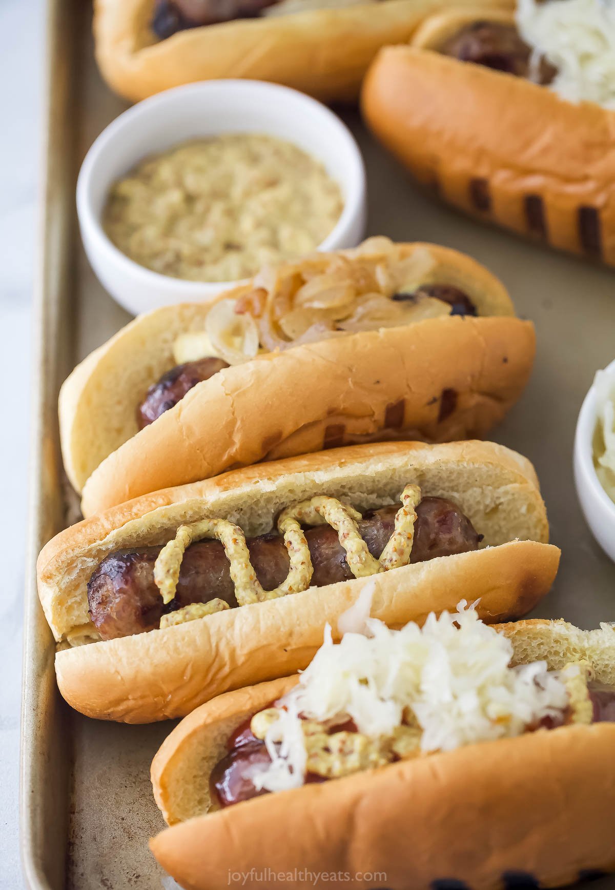 This grilled beer brats recipe with juicy sausages on toasted buns with spicy mustard and sauerkraut toppings is perfect for cookouts. Wisconsin beer brats with spicy mustard and sauerkraut.