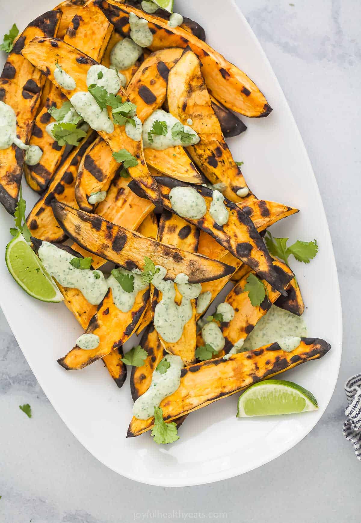 This Tex-Mex grilled sweet potatoes recipe with spicy cilantro lime crema is an easy 25-minute side for summer cookouts. Plate of grilled sweet potatoes drizzled with lime cilantro crema.