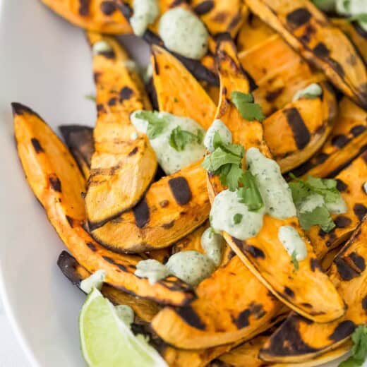 Close-up of grilled sweet potatoes with tangy cilantro lime crema and fresh cilantro on top.