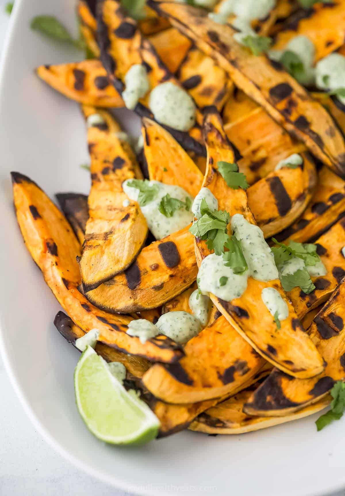 Close-up of grilled sweet potatoes with tangy cilantro lime crema and fresh cilantro on top. 