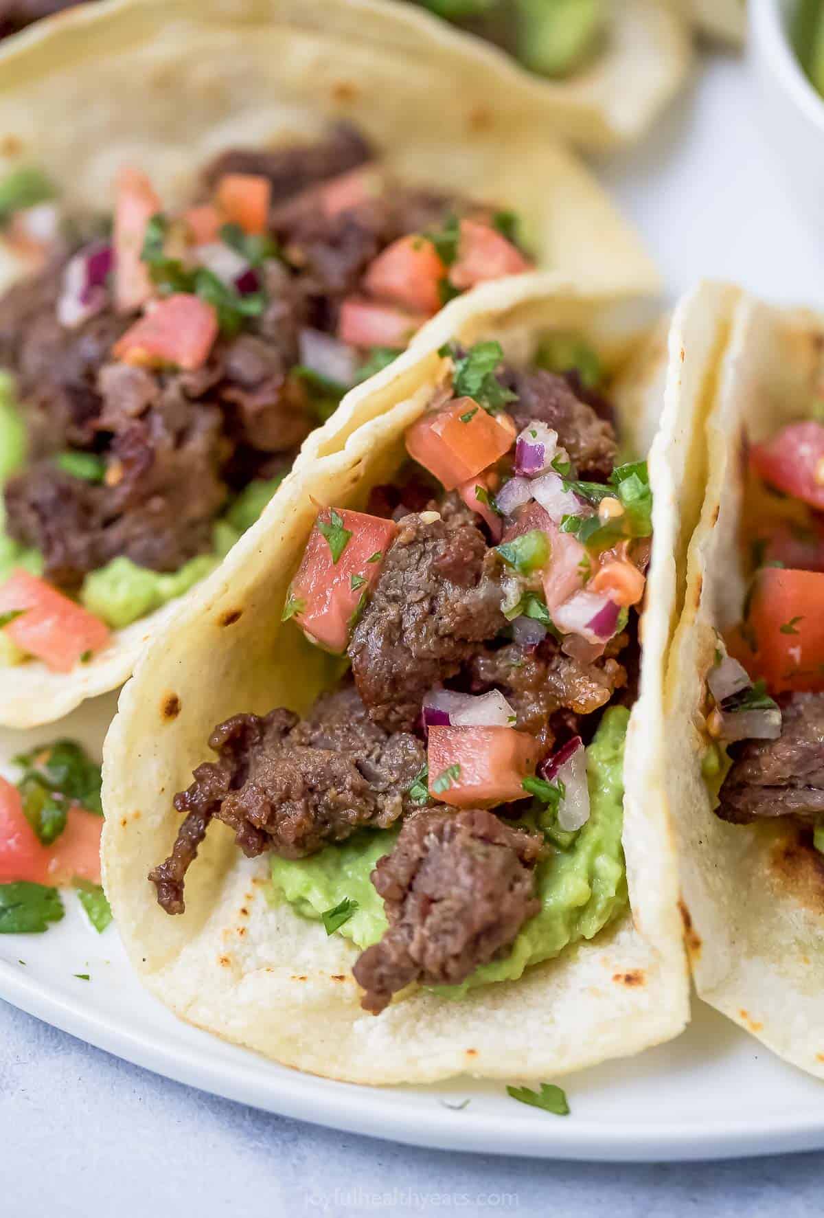 This juicy skirt steak tacos recipe will be a hit for Taco Tuesday with their tangy marinade and fresh veggie toppings. Close-up of skirt steak tacos with diced tomatoes, onions, and guacamole.