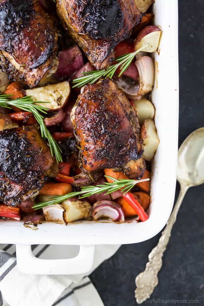 Angled photo of baked chicken with vegetables like onions, peppers, carrots, and potatoes in a baking dish. 