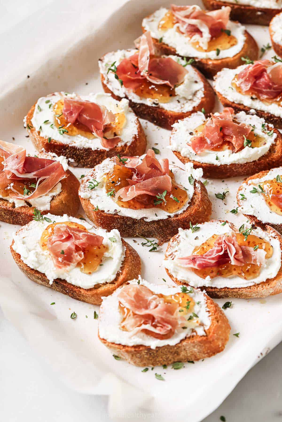 This fig-goat cheese crostini recipe with salty prosciutto is a sweet-and-savory 20-minute appetizer for the holidays. Goat cheese crostinis with fig jam and salty prosciutto on a serving platter.
