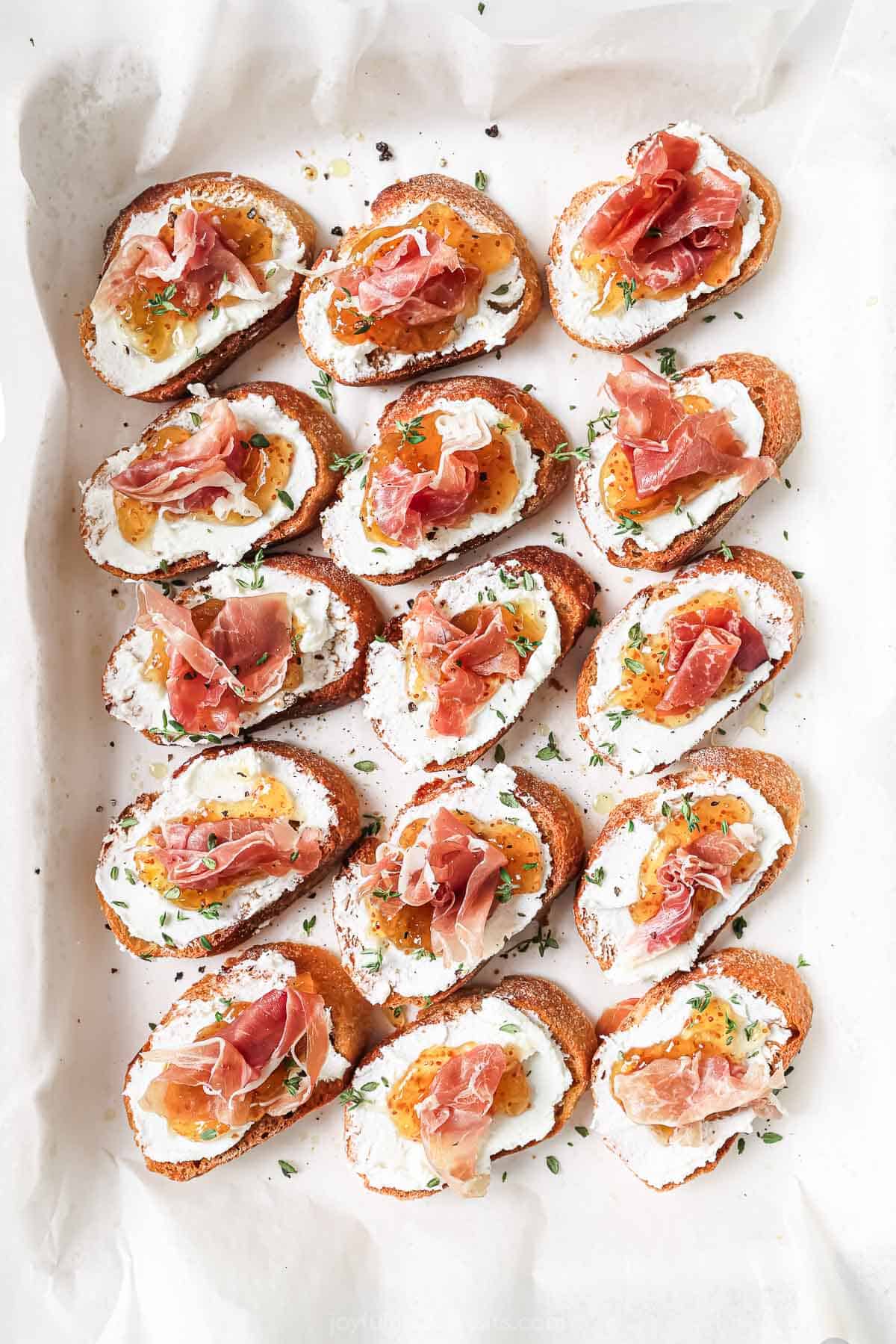 Overhead photo of Italian-inspired appetizers with toasted bread, goat cheese, jam, and prosciutto. 