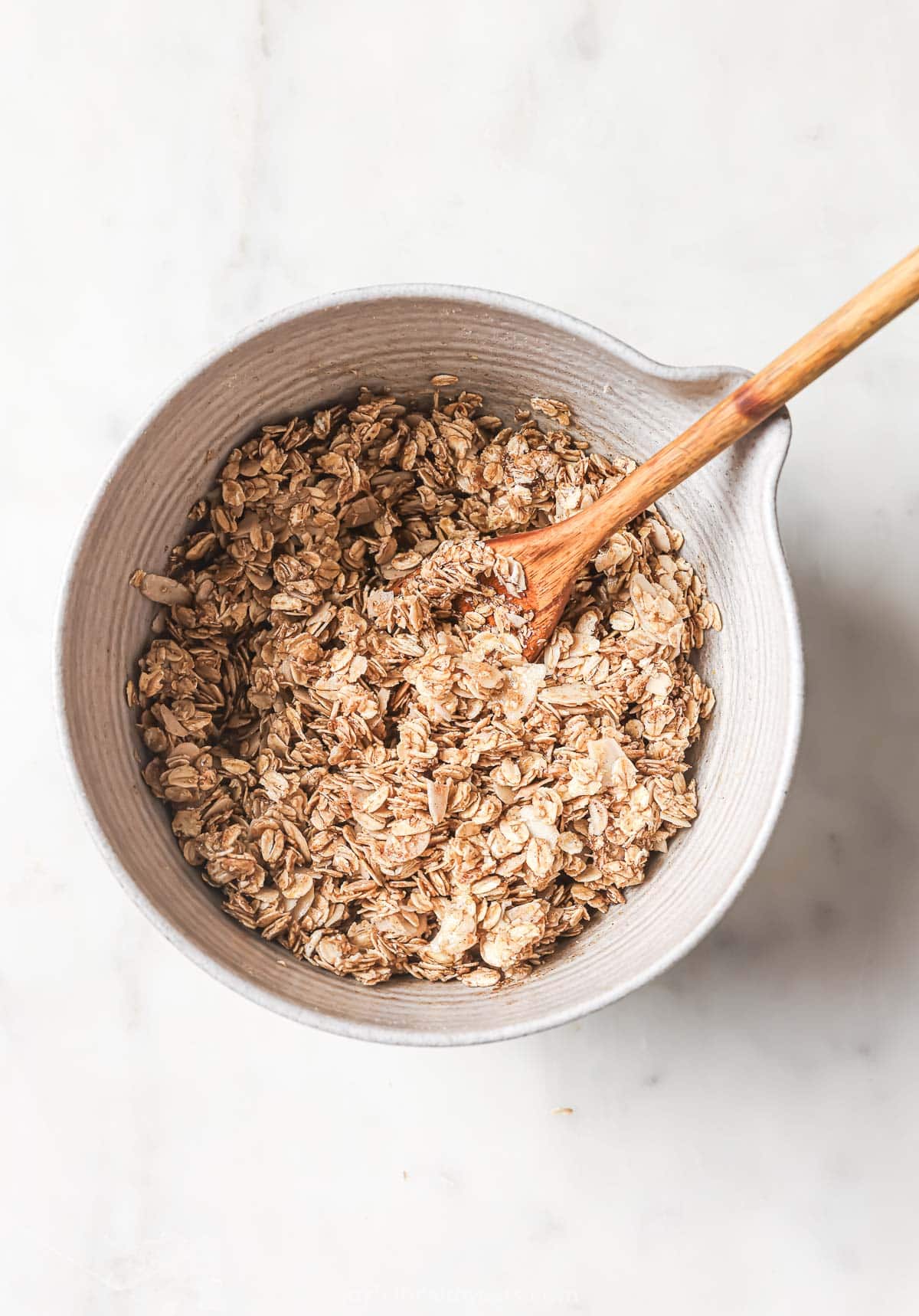Homemade granola mixture in bowl with wooden spoon