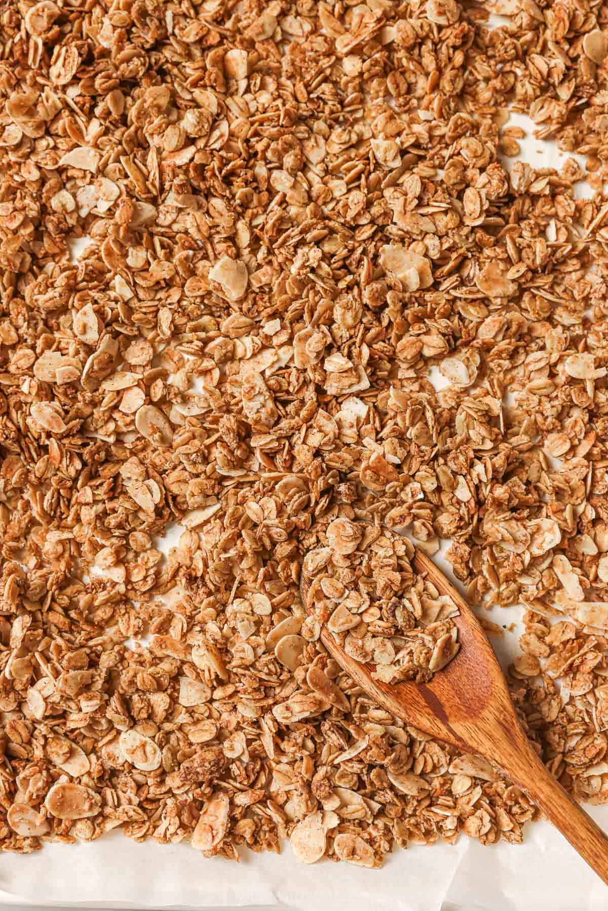 Hints of cinnamon, nutmeg, and vanilla make this homemade granola recipe a standout! Customize it with your favorite nuts and add-ins. Overhead view of granola on pan with spoon