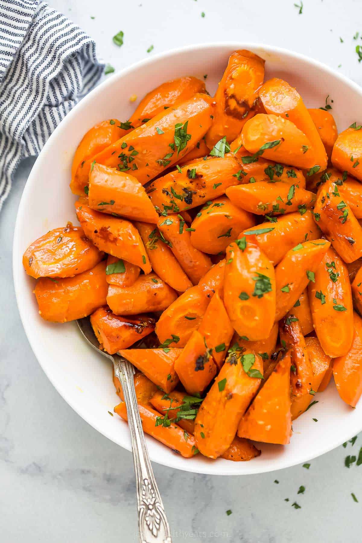 These Honey Glazed Carrots are tossed with olive oil and raw honey and roasted to perfection. It's a healthy side that's sweet and savory! a white plate with glazed and roasted carrots