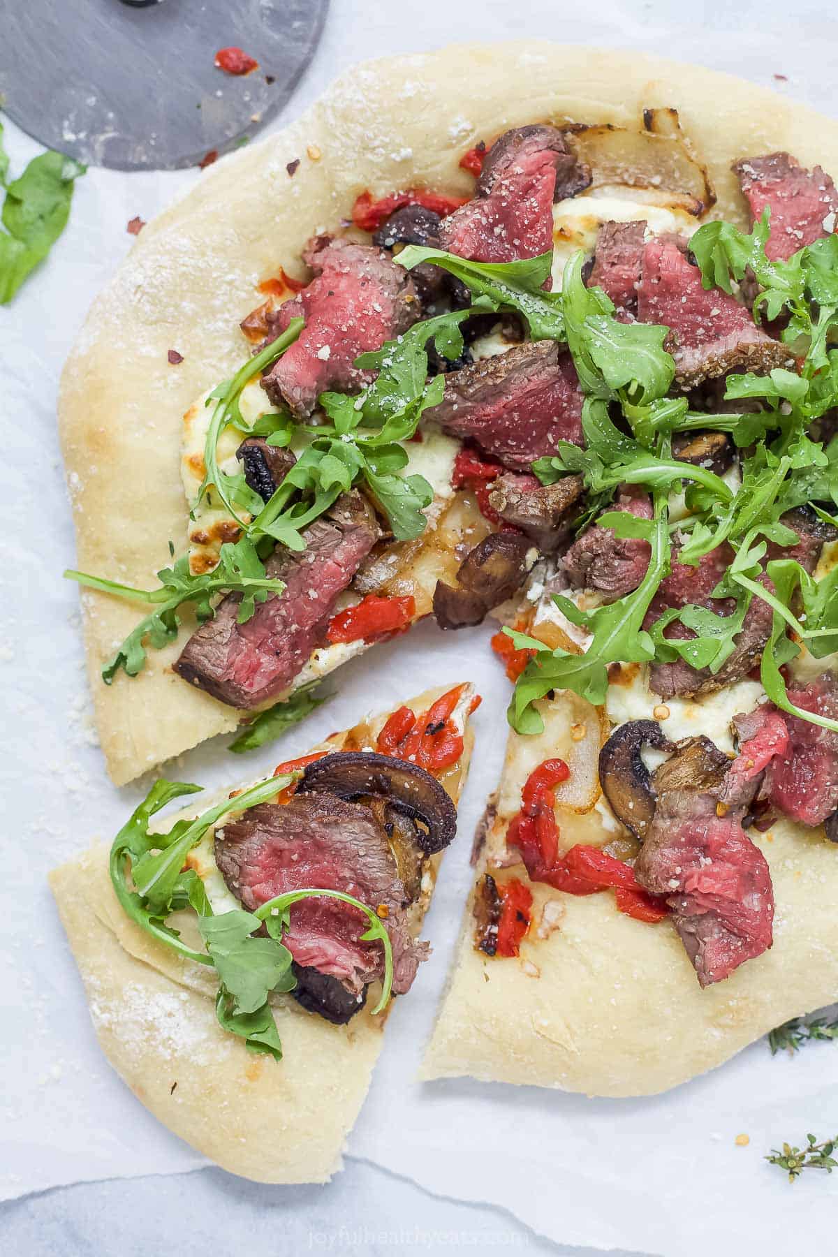 With juicy steak, whipped goat cheese, peppery arugula, and a nice mix of veggies, this homemade steak pizza is full of big flavors! Overhead view of steak pizza with one slice pulled away