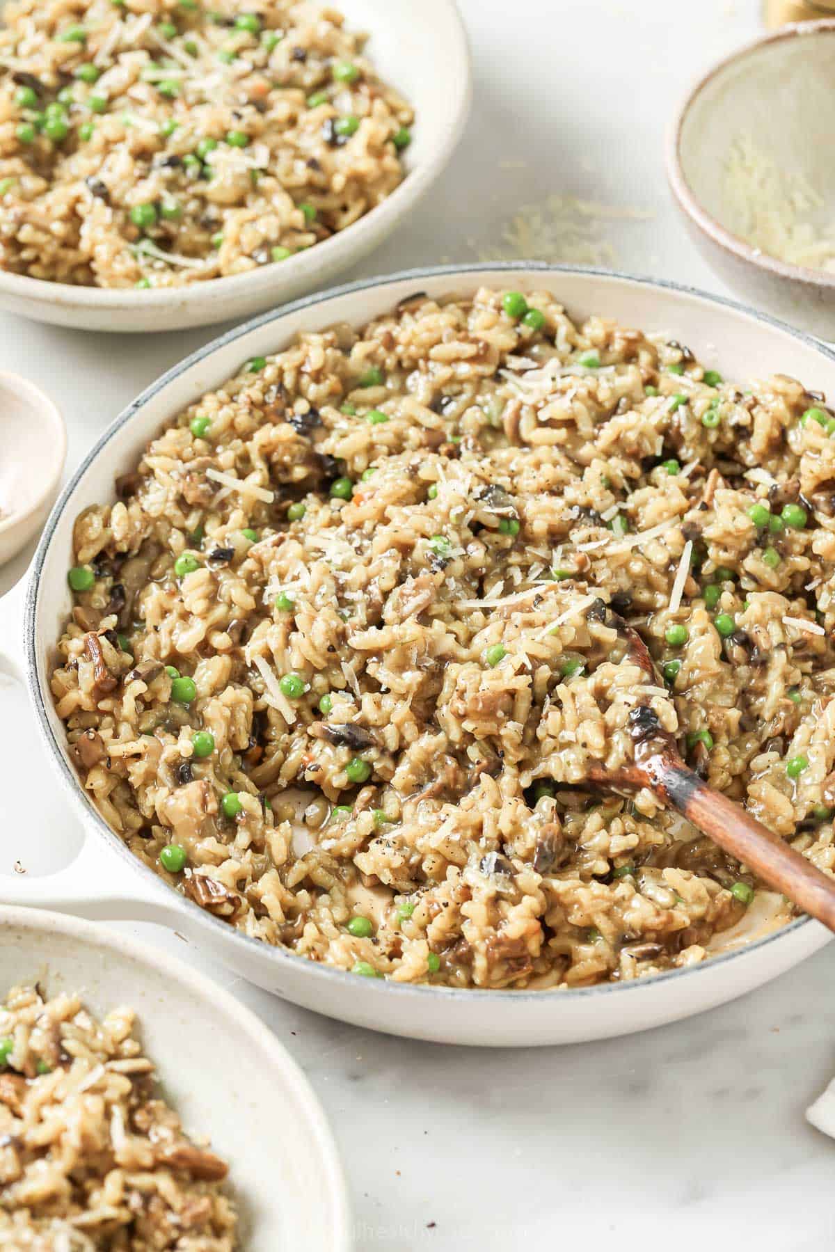 This parmesan-wild mushroom risotto recipe with sautéed onions and chewy peas is an impressive dinner for all your gatherings. Wild mushroom risotto with chewy peas and parmesan cheese in a serving bowl.