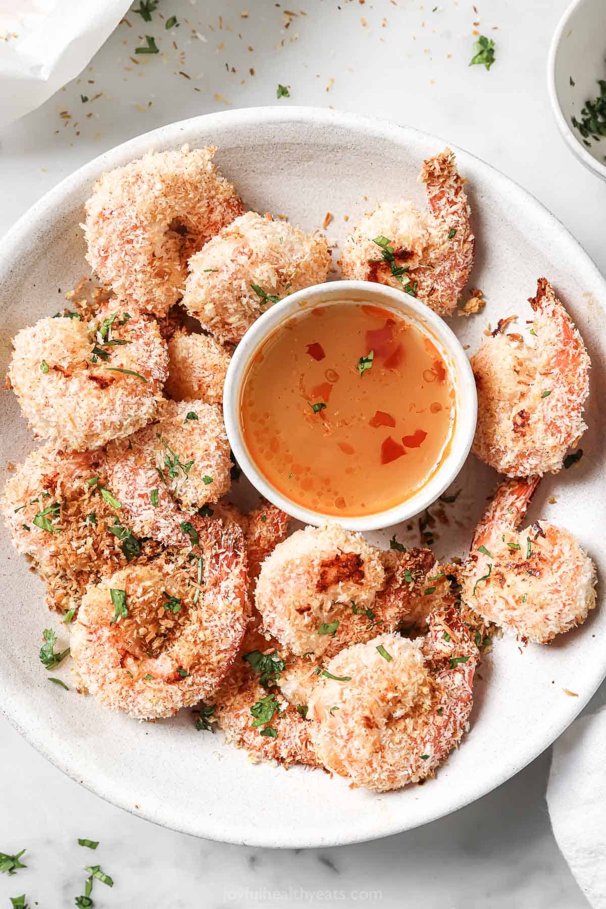 This baked coconut shrimp recipe is dipped into sweet-and-savory Thai sauce for an easy cocktail night appetizer. Serving plate with coconut shrimp and Thai ginger-garlic sauce.