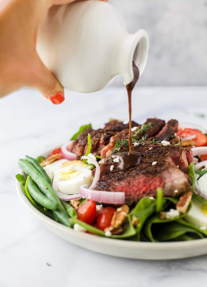Homemade balsamic dressing being poured over a freshly-made salad on a plate