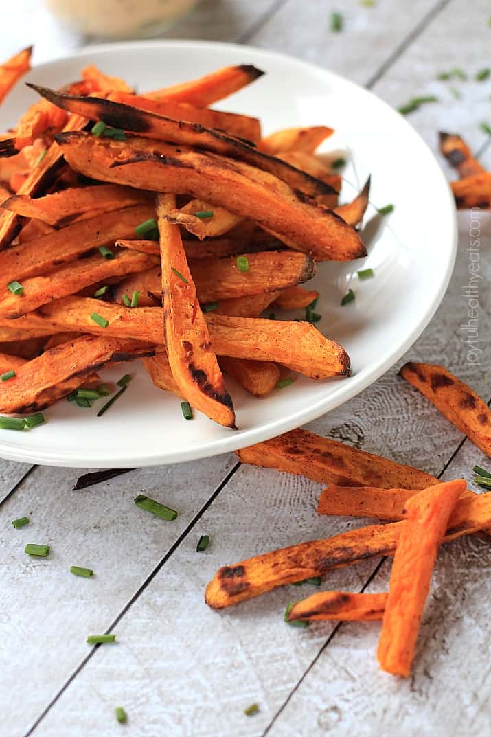A plate of sweet potato fries on a table with a few loose fries beside the plate.