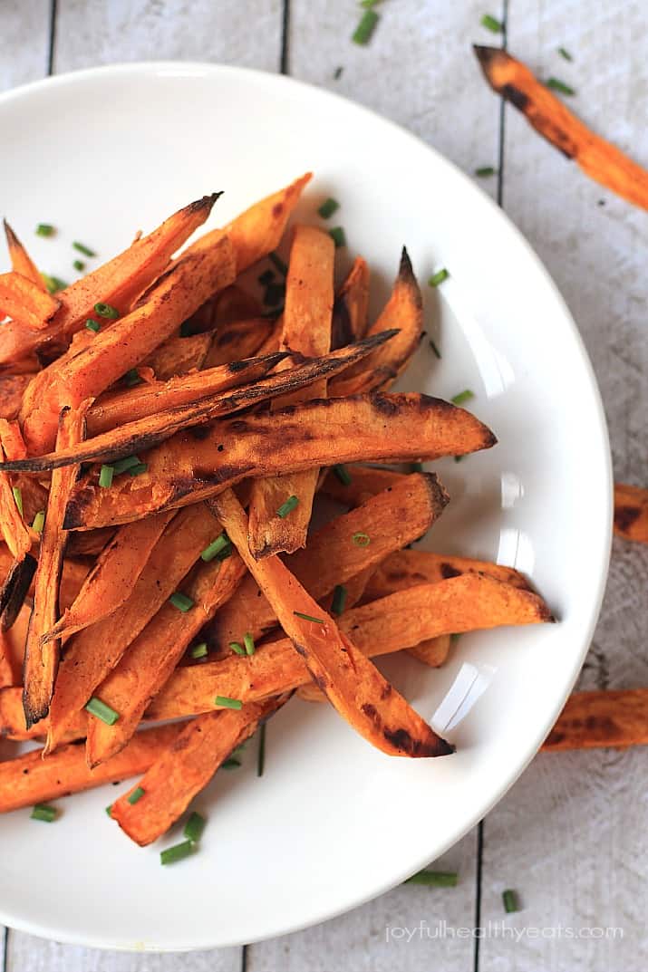A close-up shot of crispy sweet potato fries piled onto a shiny white plate.