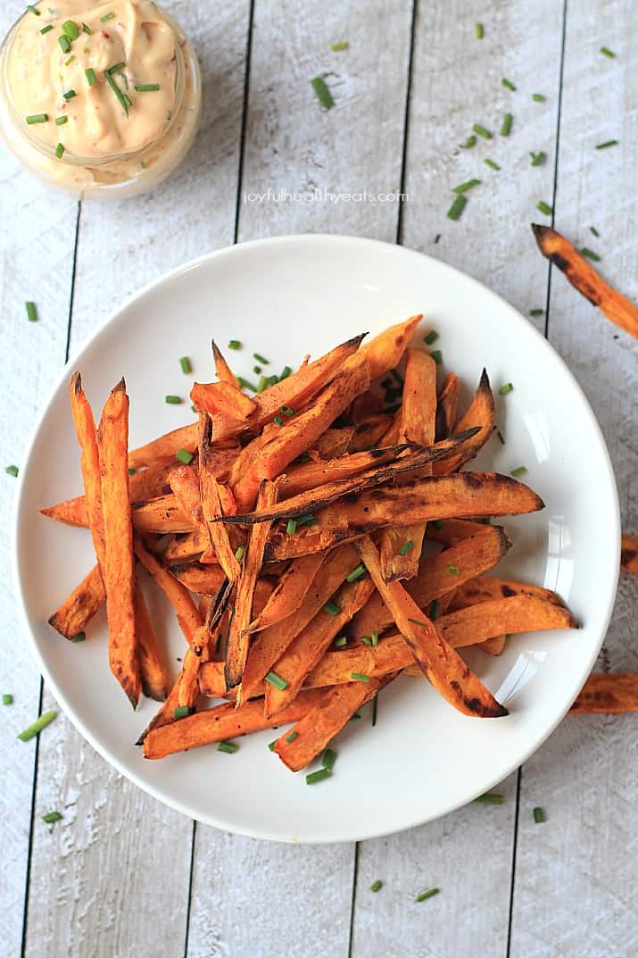 A plate containing sweet potato fries garnished with chopped fresh chives.