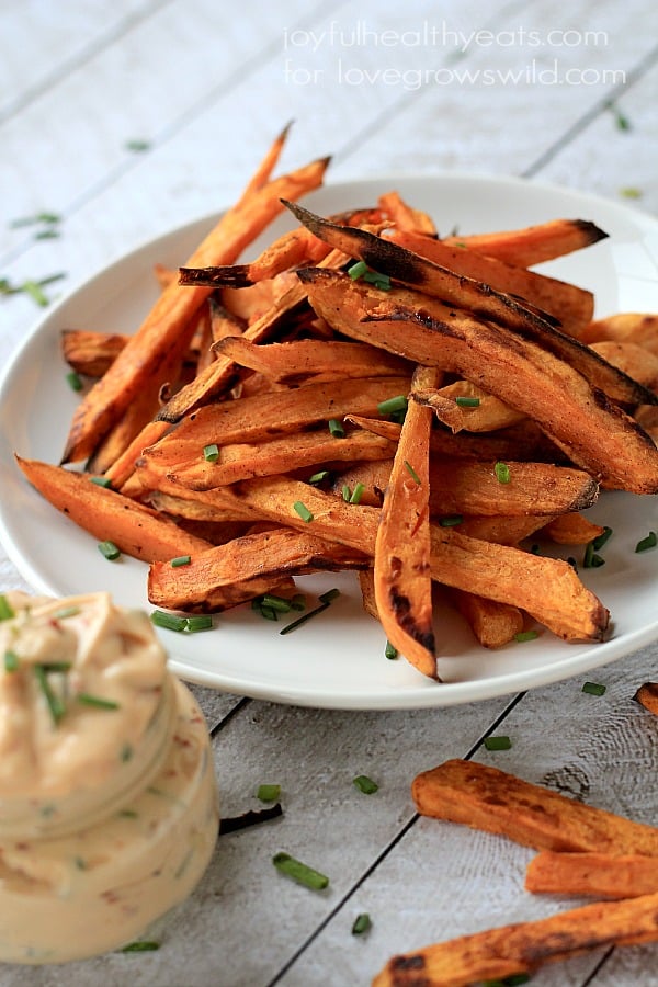 Sweet potato fries piled onto a plate with a small jar full of chipotle lime sauce in the foreground.