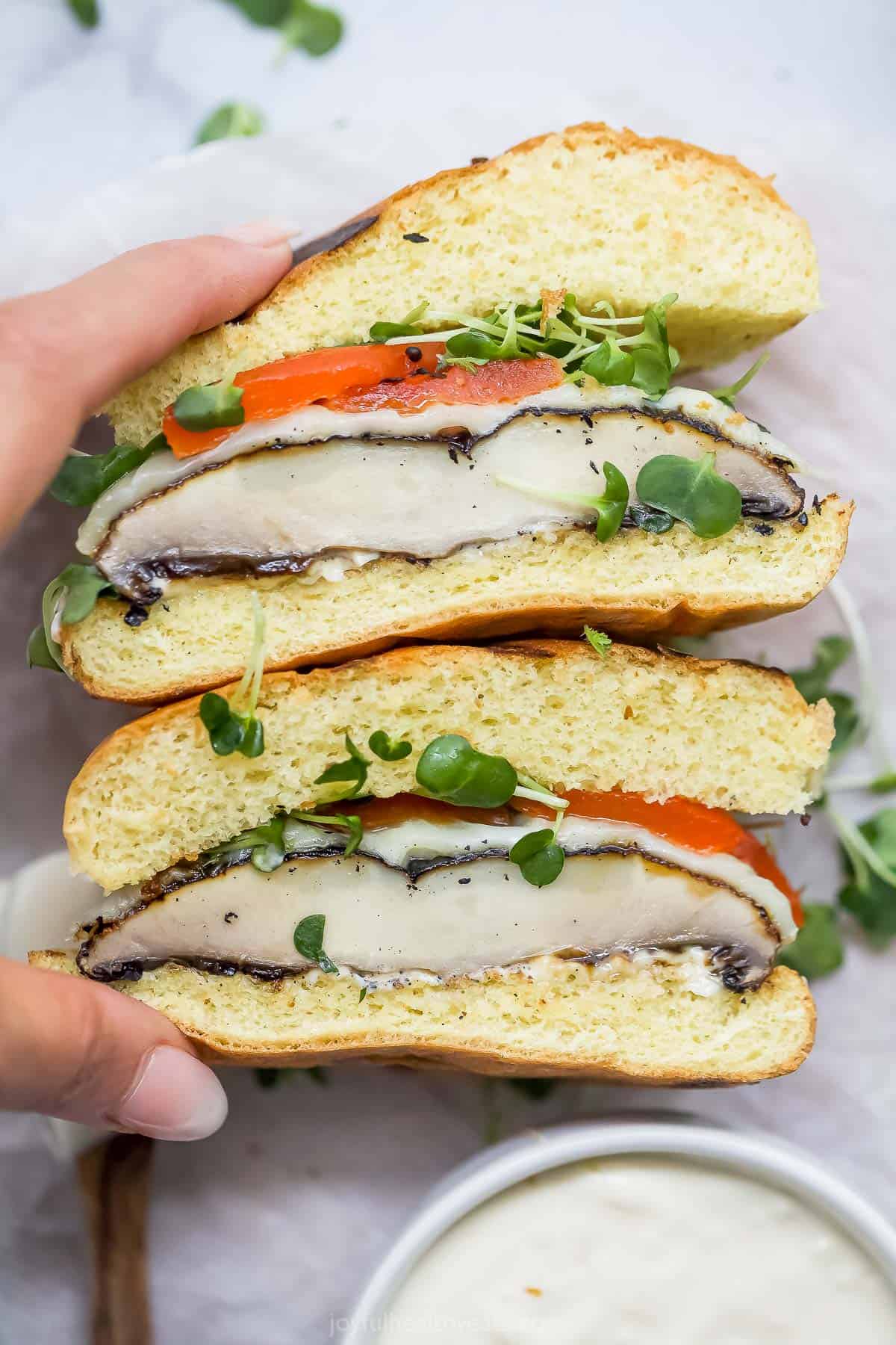 Hand holding two halves of a portobello mushroom sandwich