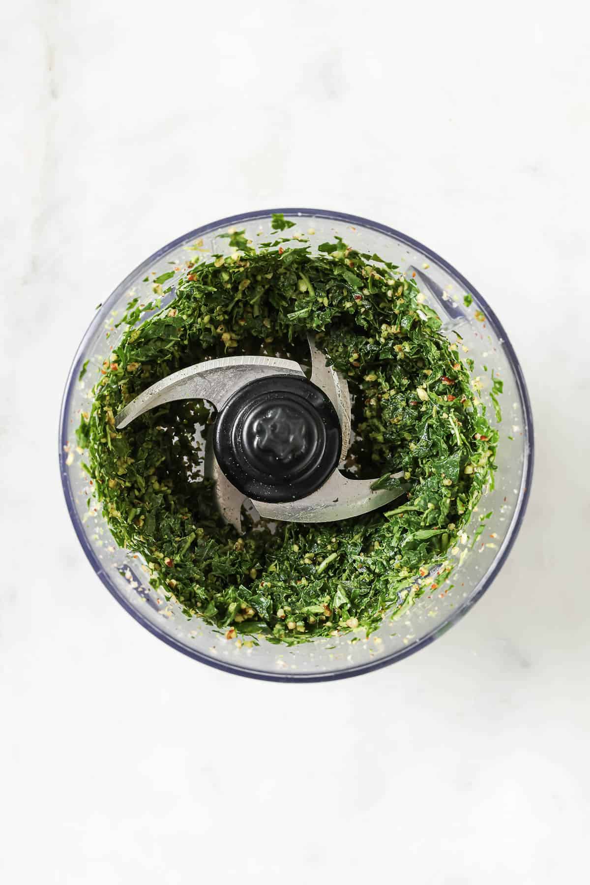 Chopped basil, nuts, and other ingredients for pesto in food processor bowl