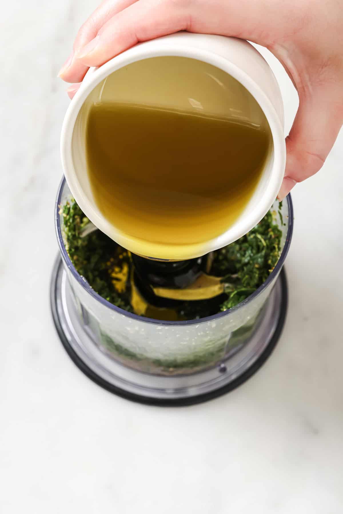 Pouring oil into food processor to make homemade basil pesto