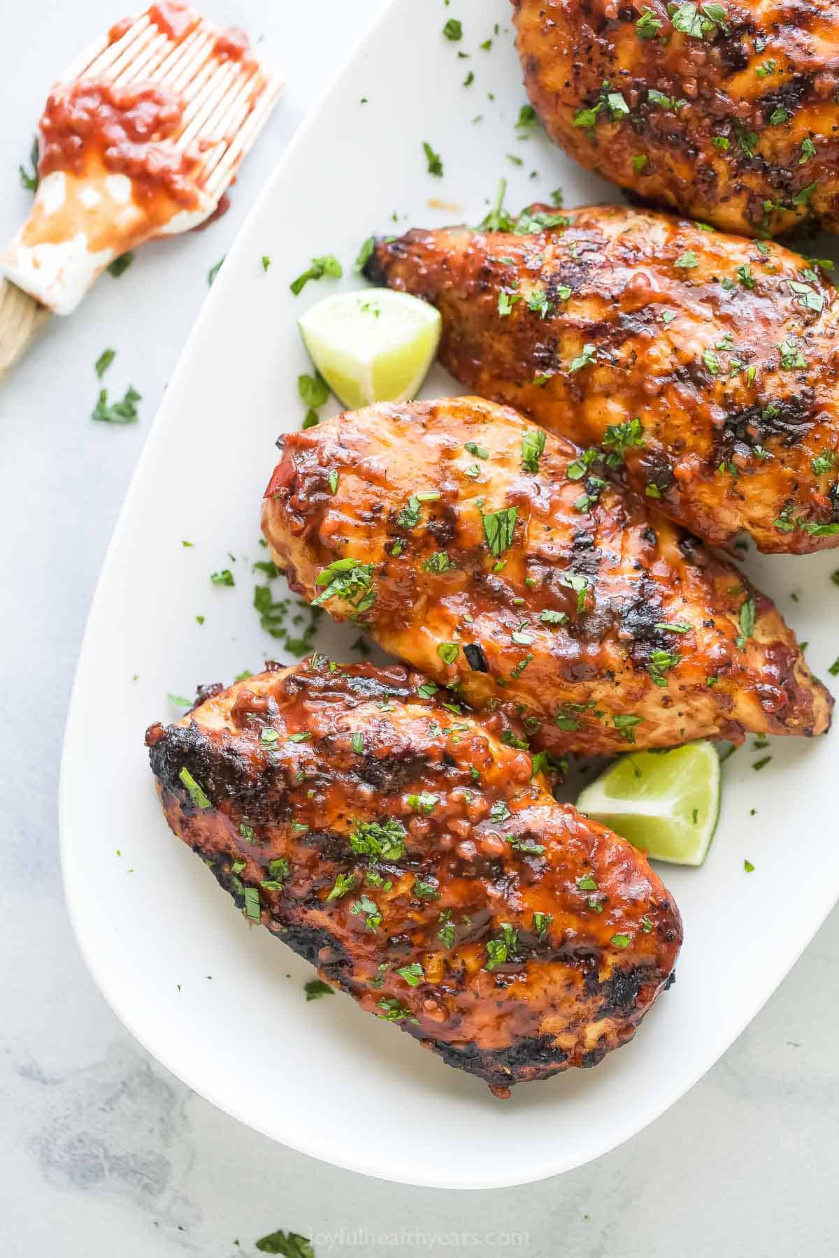 This sweet-and-savory, juicy grilled chicken recipe with smokey raspberry-chipotle BBQ sauce is an easy 15-minute dinner. Grilled chicken with sweet-and-savory BBQ sauce, fresh cilantro, and lime wedges.