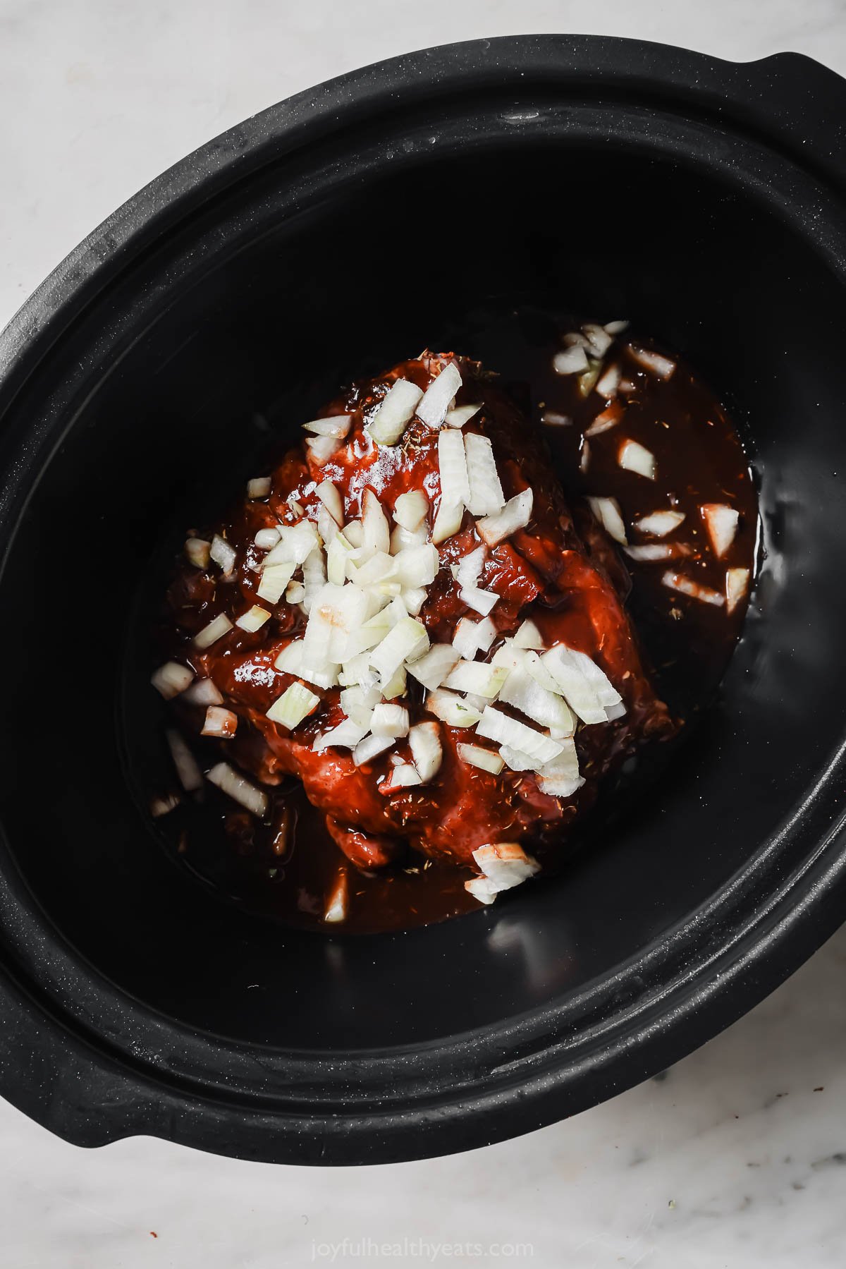 Pork in the crock pot with  the homemade sauce and chopped onions on top. 