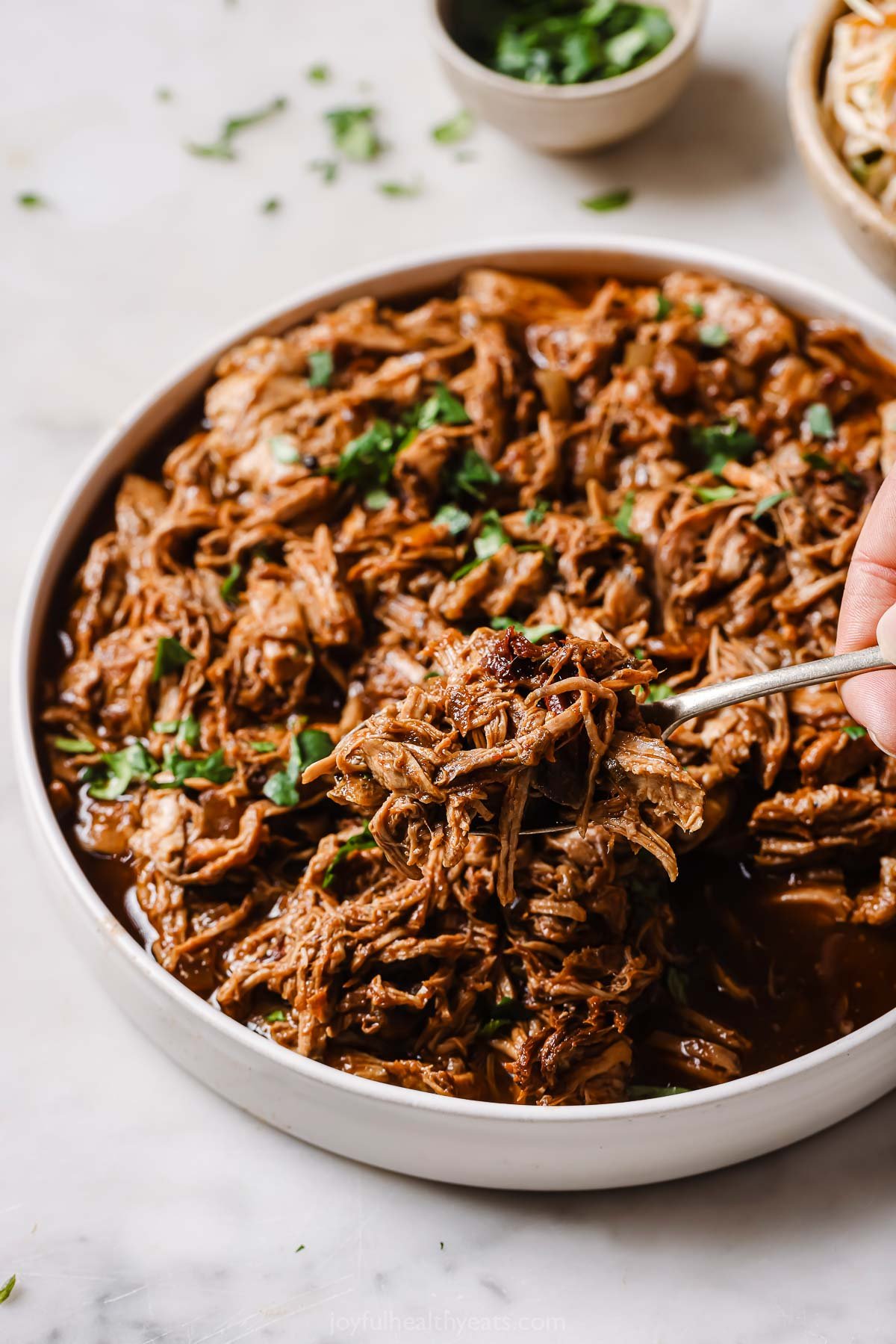 This crock pot pulled pork recipe with caramelized onions and honey-chipotle sauce is perfect for filling your sliders this summer. Grabbing some saucy pulled pork with a fork.