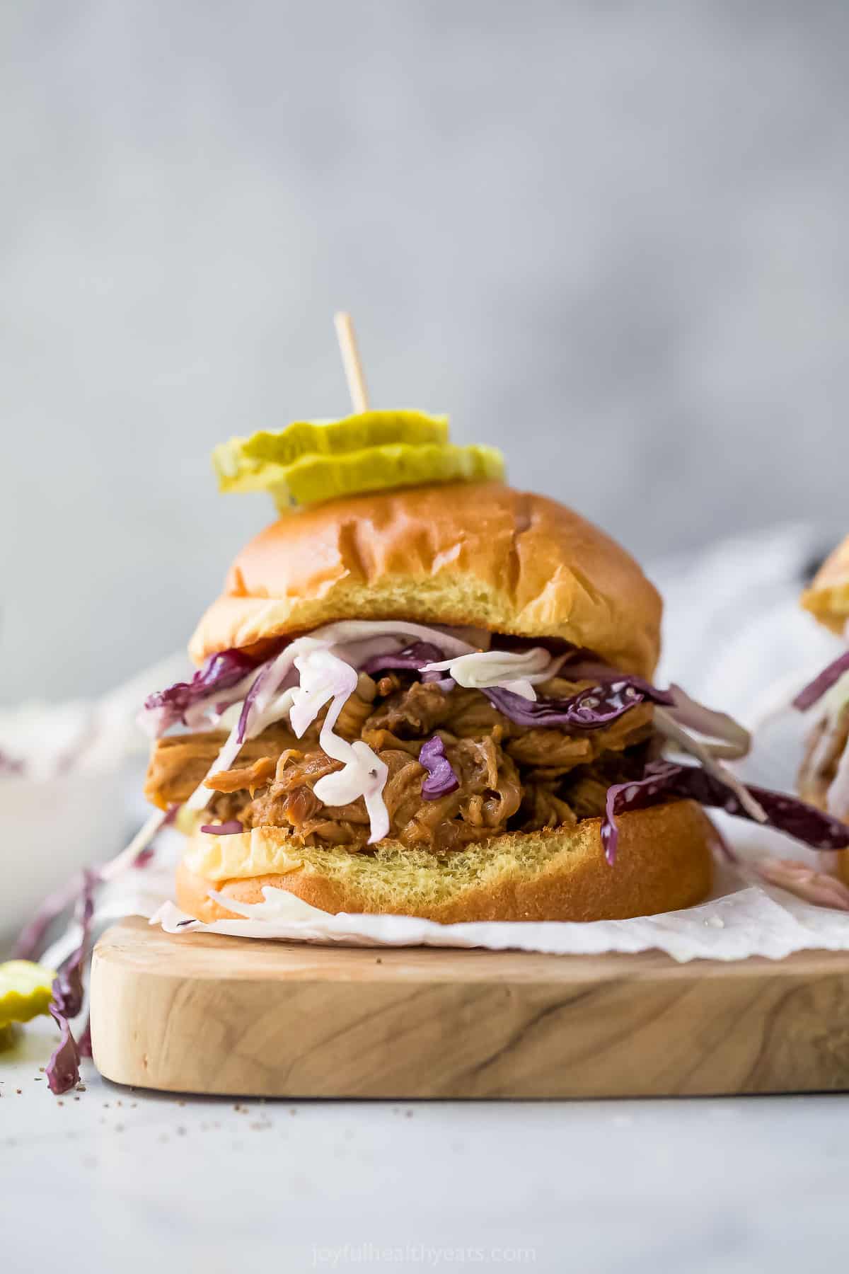 Piled high with honey balsamic pork and crunchy cabbage coleslaw, these easy pulled pork sandwiches are the perfect game day dinner! Pulled pork sandwich with coleslaw and pickles on top
