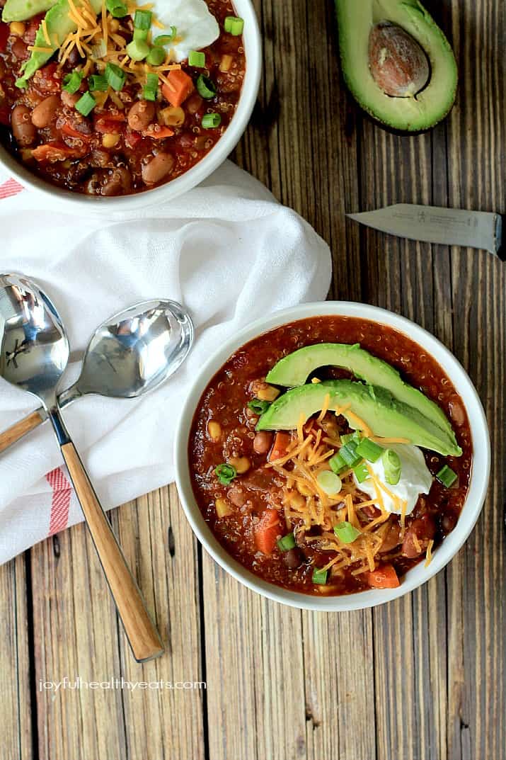 This crock pot vegetarian chili recipe is loaded up with veggies, quinoa, and three different types of beans. It's so thick and hearty! Two bowls of chili with avocado slices on top.