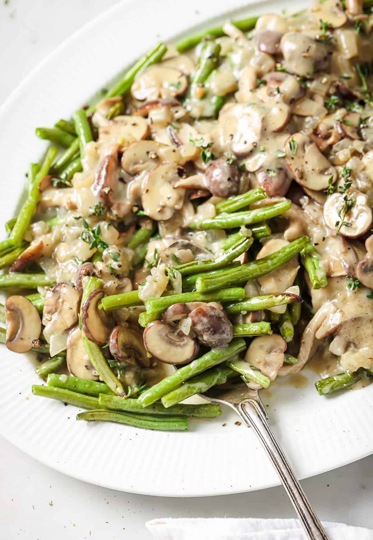 This roasted green beans and mushrooms recipe with homemade creamy mushroom-thyme sauce is a quick holiday side you'll love. Serving plate of roasted green beans and mushrooms with coconut-thyme sauce.