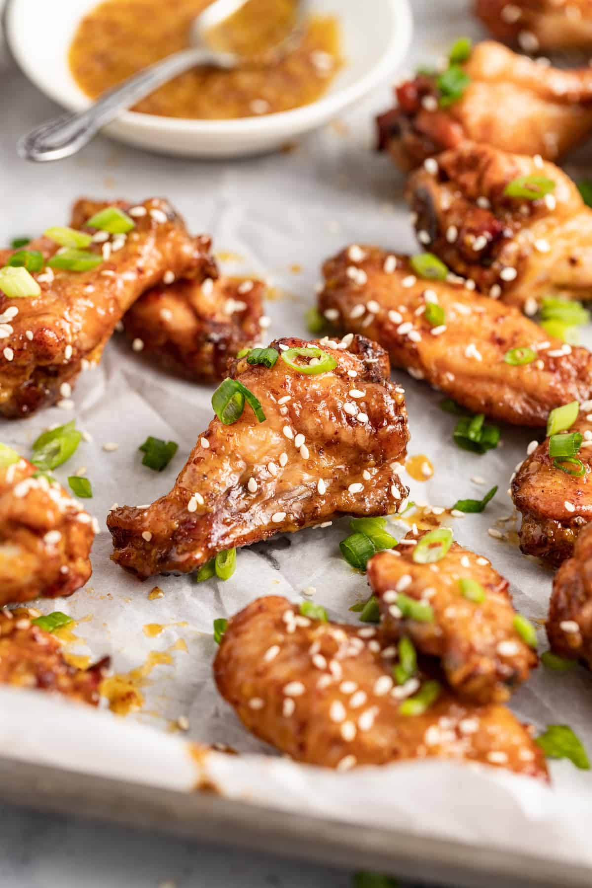 Honey Mustard Baked Chicken Wings are a fun appetizer to make for your next party. It has an easy honey mustard saucethat everyone will love. baked chicken wings on a lined sheet tray with sesame seed and herb garnish