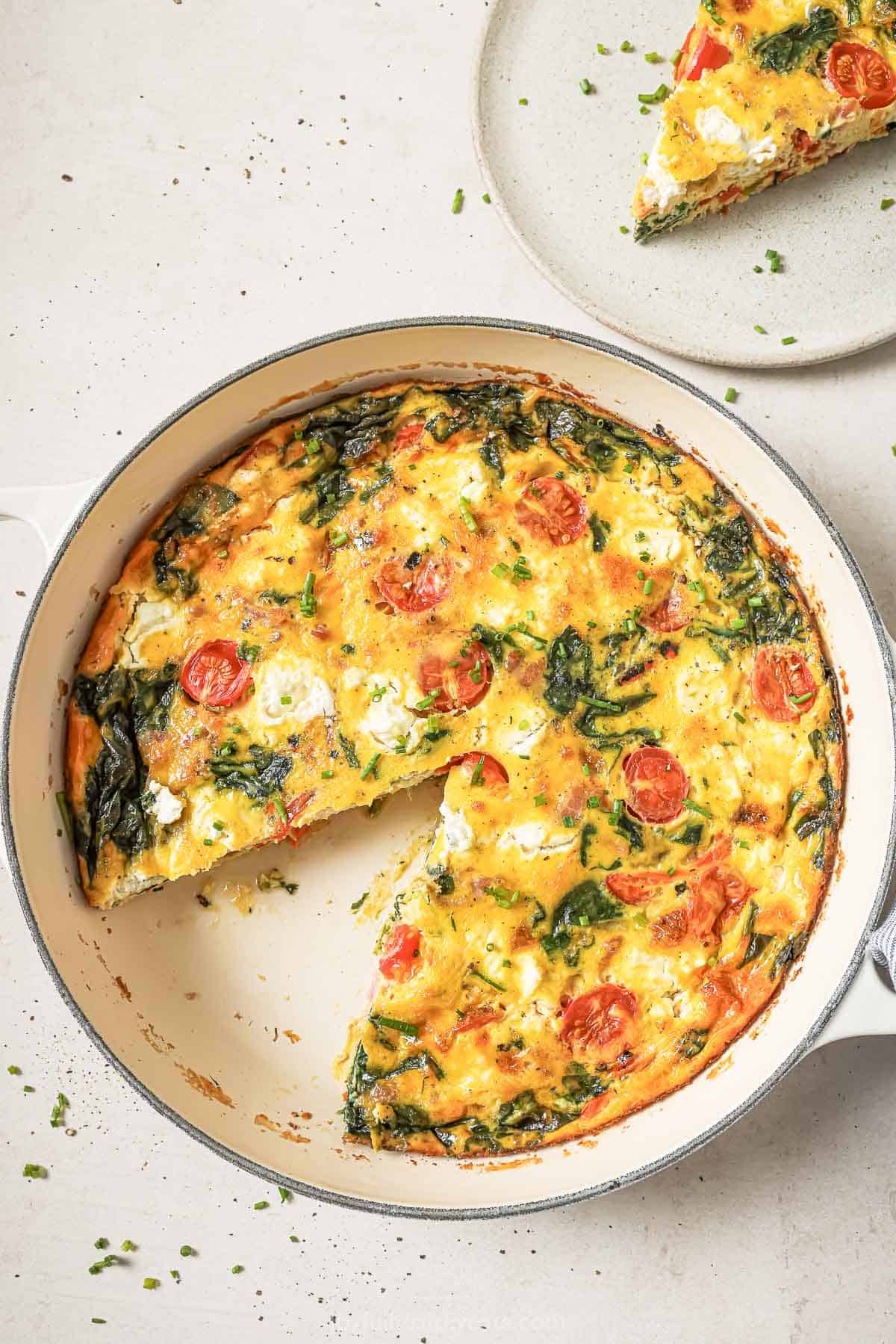 Overhead view of cheesy bacon spinach frittata in pan with one slice removed
