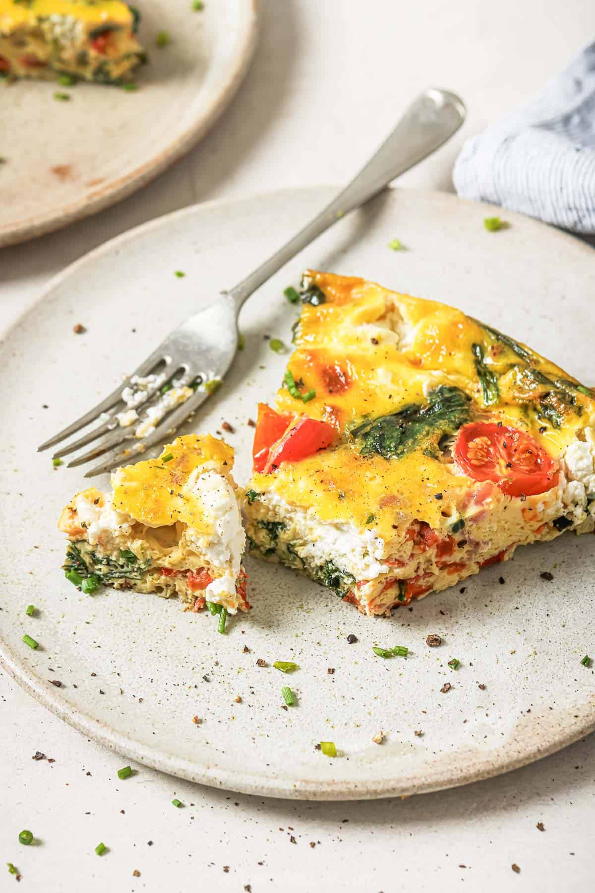 This cheesy bacon spinach frittata is done in just 30 minutes! With goat cheese, roasted red peppers and bacon, it’s packed with flavor. Cheesy bacon spinach frittata on plate with fork