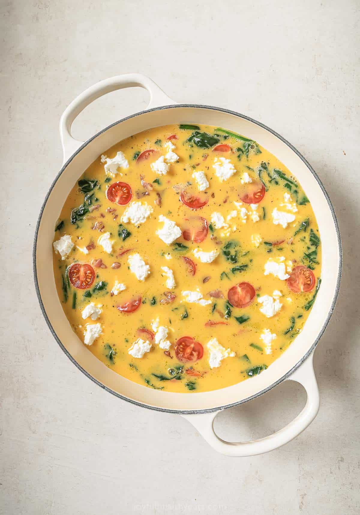 Tomatoes and goat cheese added to frittata before baking