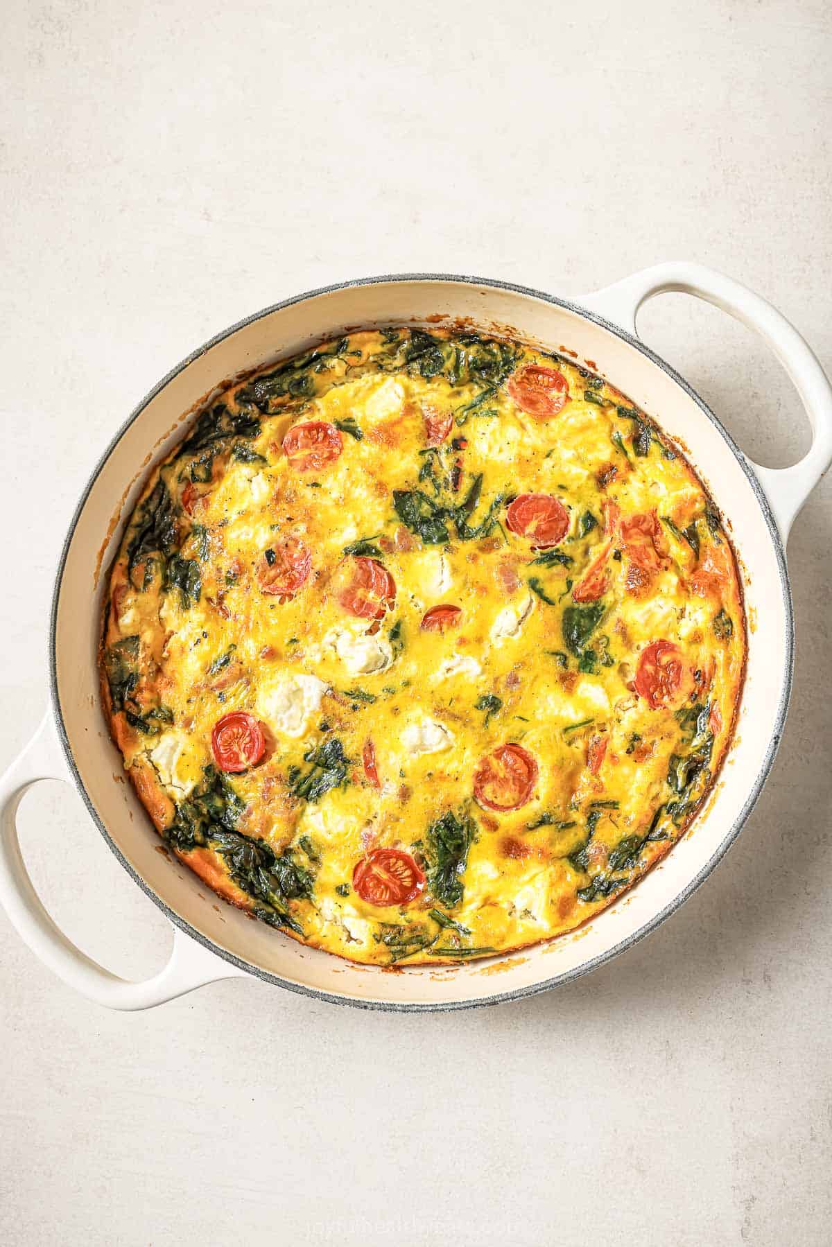 Overhead view of cheesy bacon spinach frittata baked in skillet