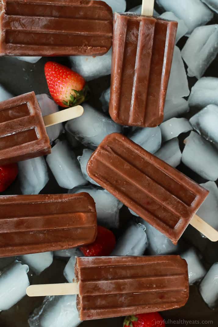 Made without any sugar or dairy, these fudgy and refreshing Chocolate Banana Popsicles are bound to become your favorite summer treat. Six dairy-free popsicles on top of a layer of ice and fresh strawberries