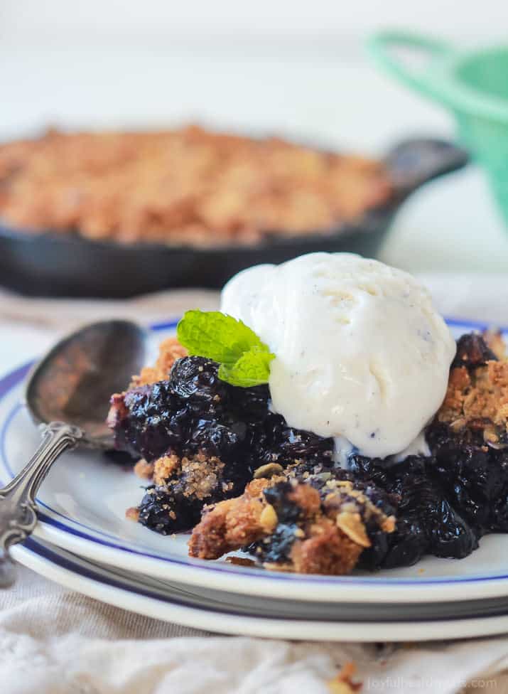 Ginger blueberry crisp on top of a stack of two plates with a metal spoon beside it.