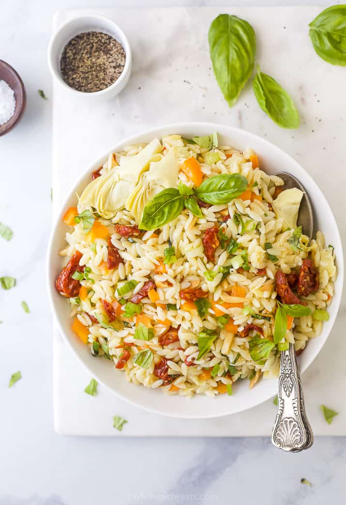 Mediterranean Orzo Pasta Salad A Bowl of Orzo Salad on a Countertop with Spices and Herbs