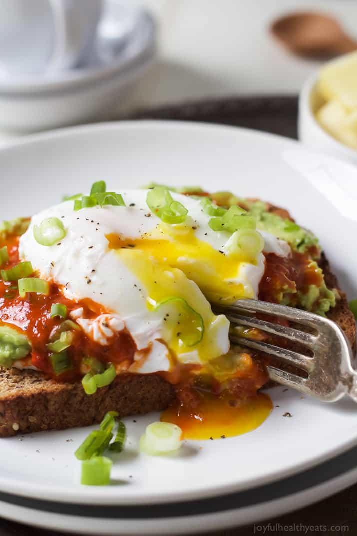 This easy avocado toast with poached egg recipe has spicy harissa, creamy ricotta, and crunchy green onions for the perfect brunch bite. Slicing into the avocado toast with poached egg.
