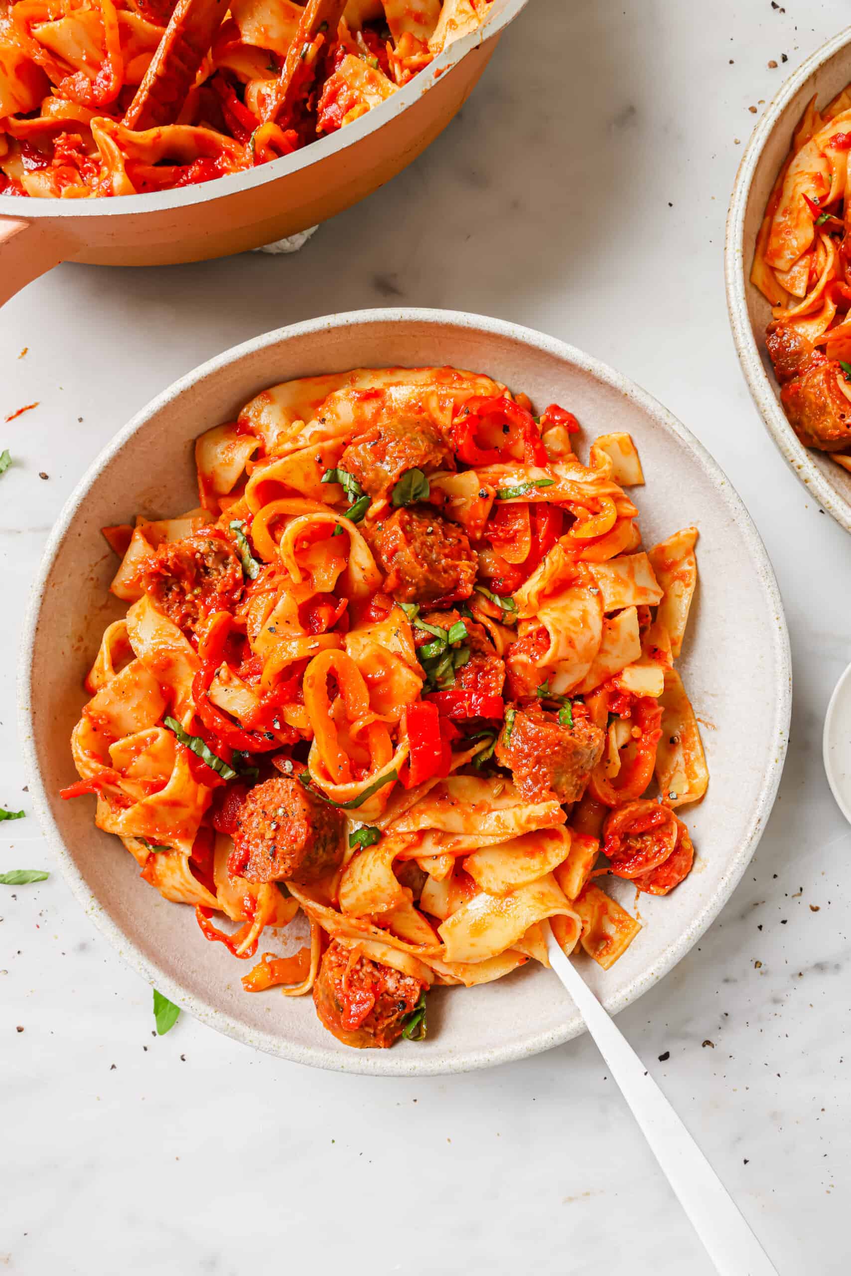 This tomatoey pappardelle Pasta is a classic Italian comfort food full of juicy sausage, sweet peppers, and lots of parmesan cheese. Pappardelle pasta in a bowl with parmesan and basil.