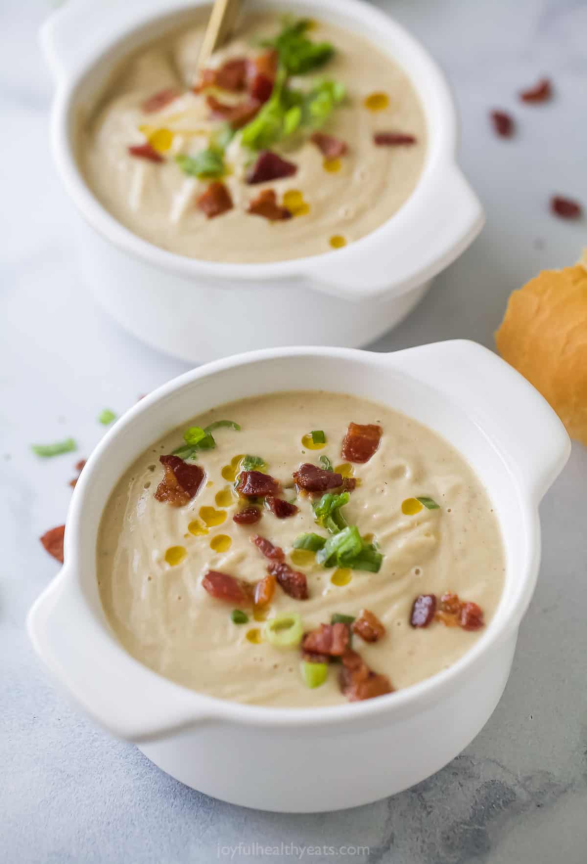 This buttery roasted cauliflower soup with crispy bacon, green onions, and spicy chili oil is an easy one-pot dinner. Two bowls of hearty cauliflower soup topped with bacon, green onions, and chili oil.